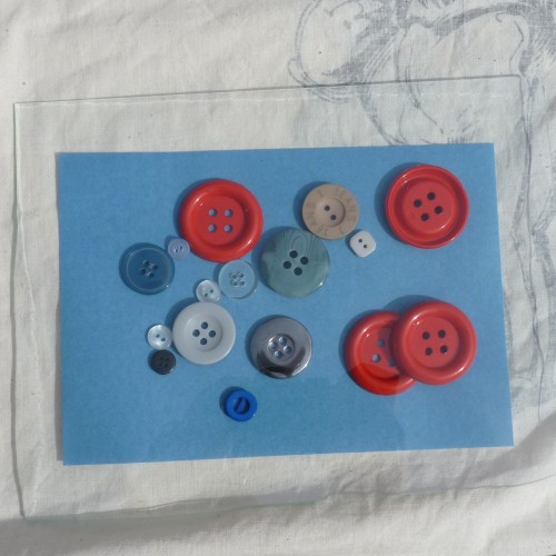 A selection of buttons on sun print paper under sheet of glass